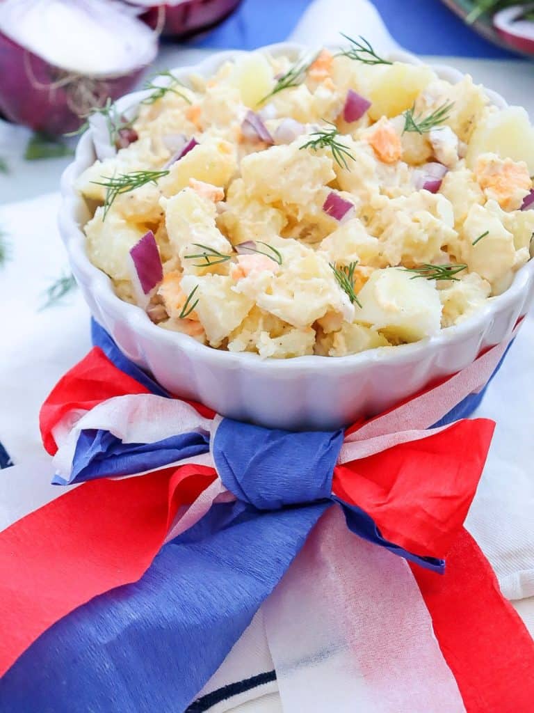 white ceramic bowl of potato salad with red, white and blue ribbon wrapped around the bowl