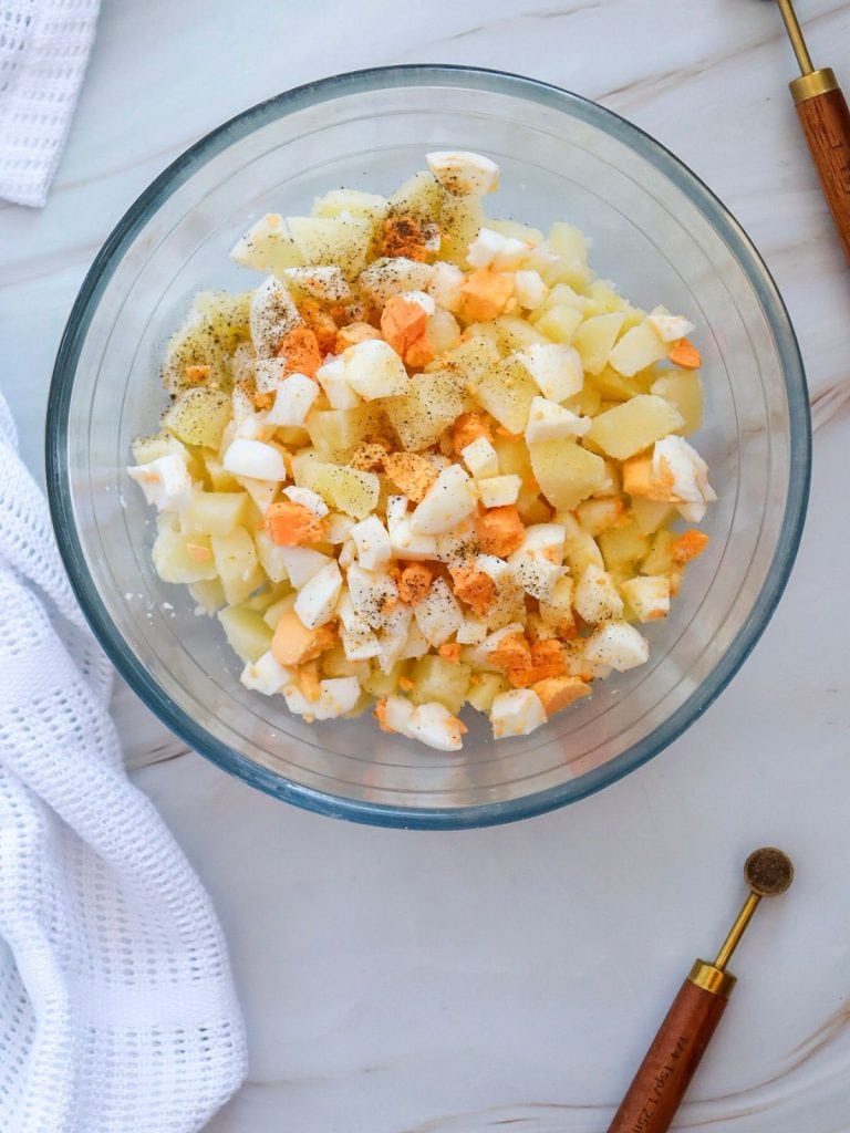 A glass mixing bowl with cubed potatoes and chopped hard boiled eggs.
