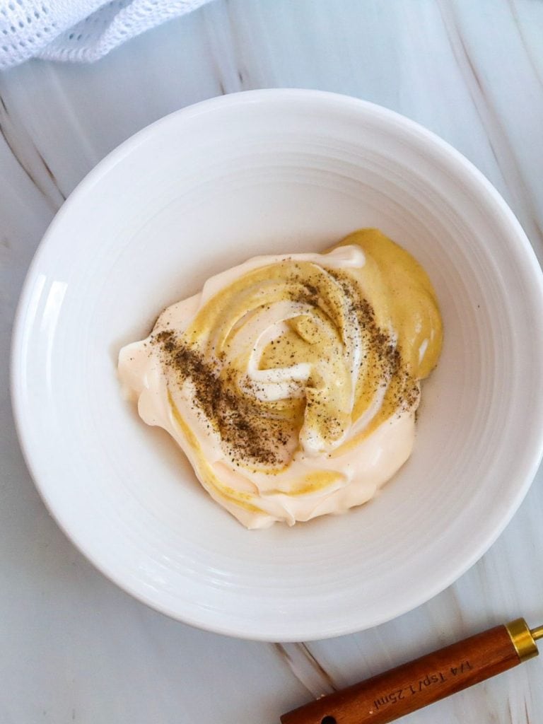 A white ceramic bowl filled with mayonaise, mustard and salt and pepper.