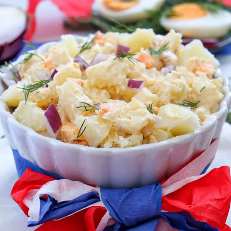white ceramic bowl of potato salad with red, white and blue ribbon wrapped around the bowl