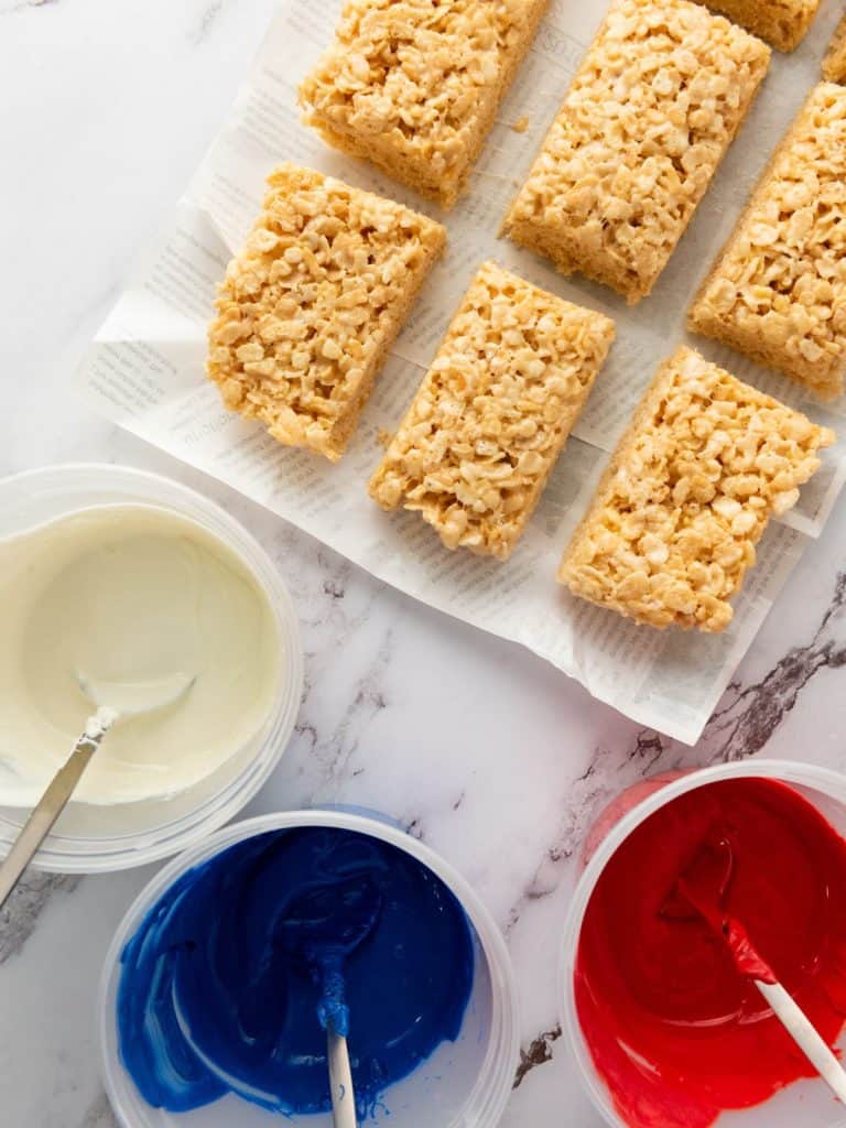 3 bowls of melted candy melts and plain rice krispie treats cut and ready to be decorated