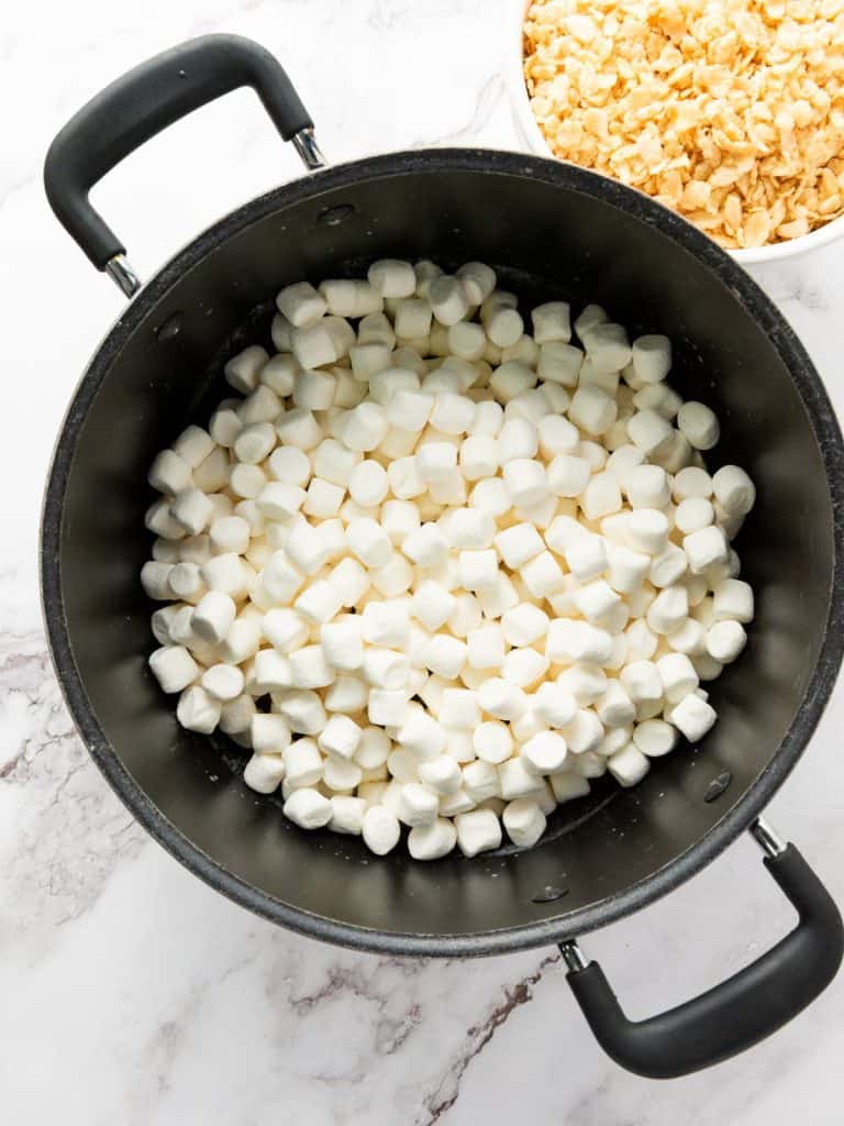 Marshmallows added to melted butter to melt for rice krispie treats in a large pot