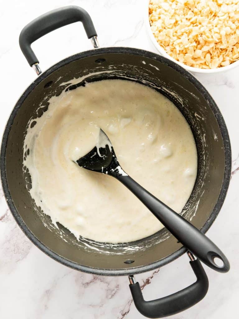 A large cooking pot with butter and melted marshmallows and a black plastic spoon