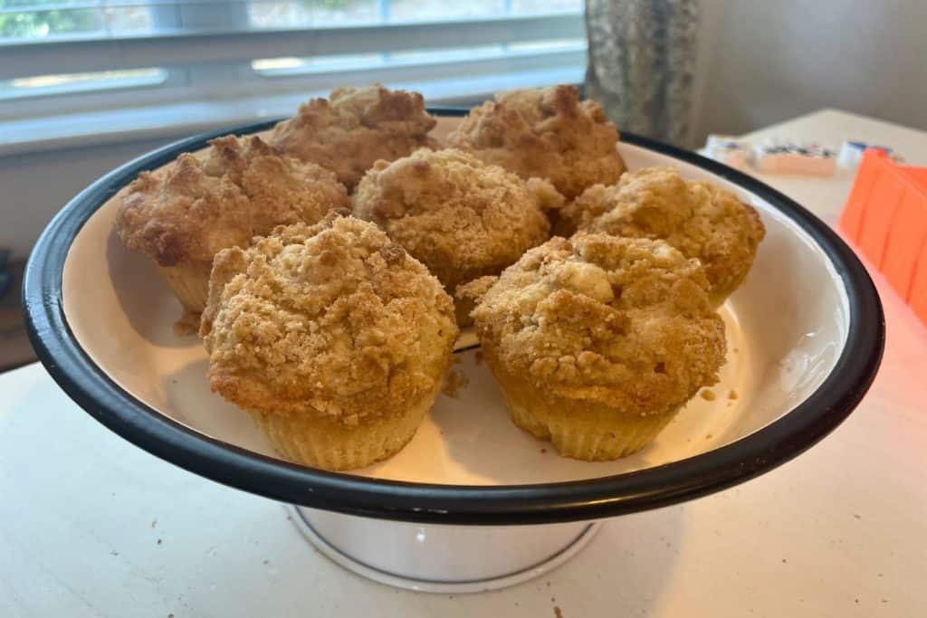 Apple cinnamon streusel crumble muffins on a white pedestal platter on a table.