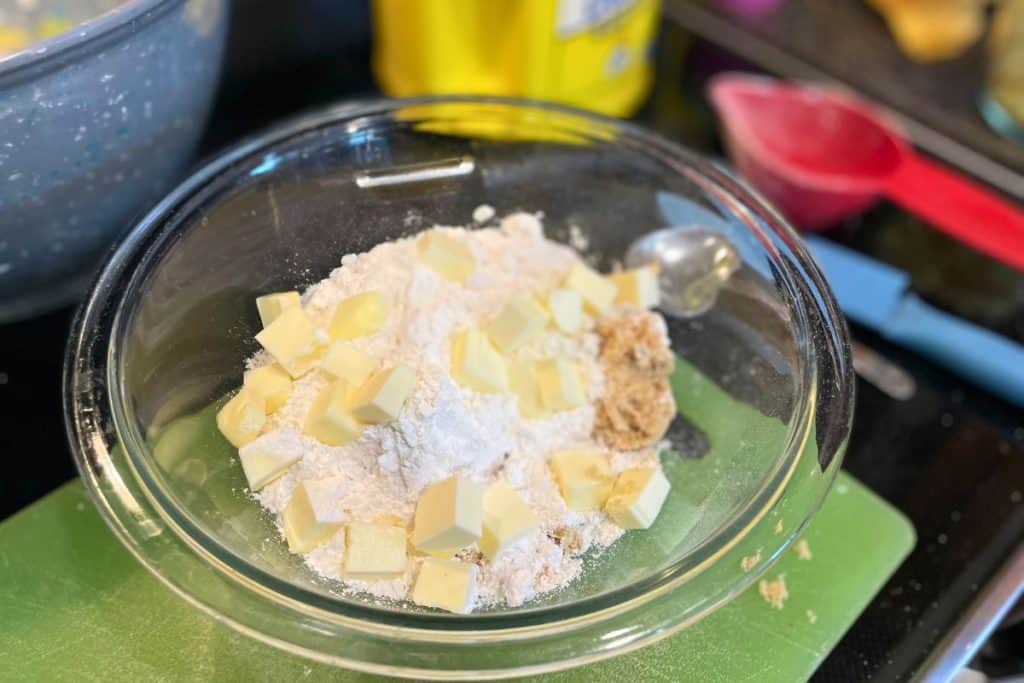 The crumble topping ingredients in a glass bowl including brown sugar, flour and cubes of cold butter