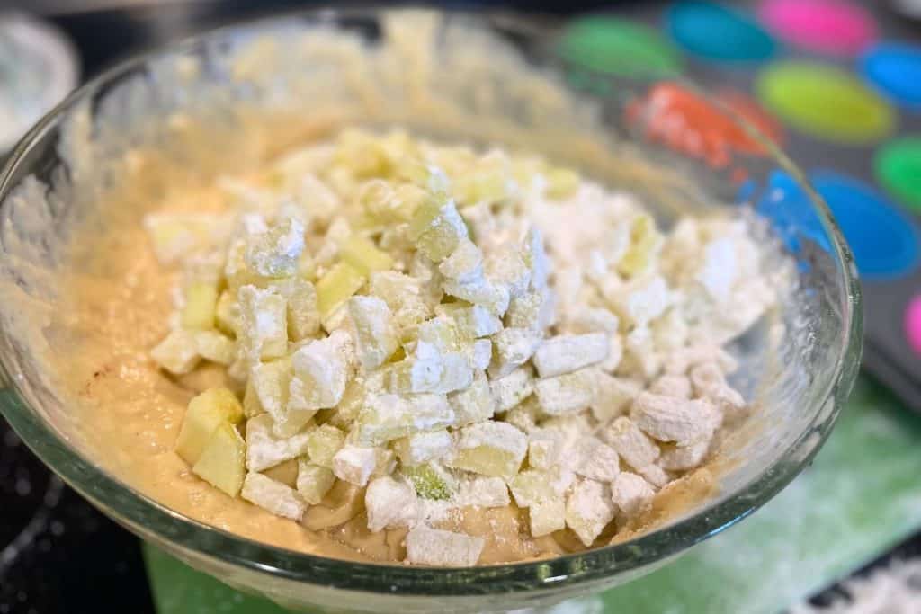 Flour-coated apples poured into a glass bowl of apple muffin batter