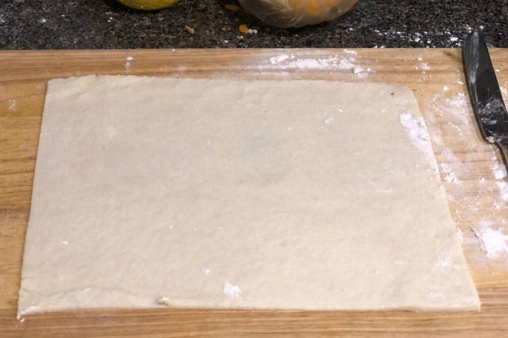Rolled out pie crust dough on a wooden cutting board with flour