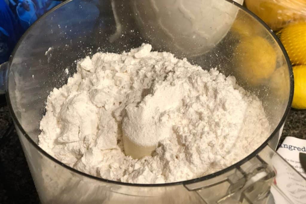 Flour and sugar poured into the container of a food processor.