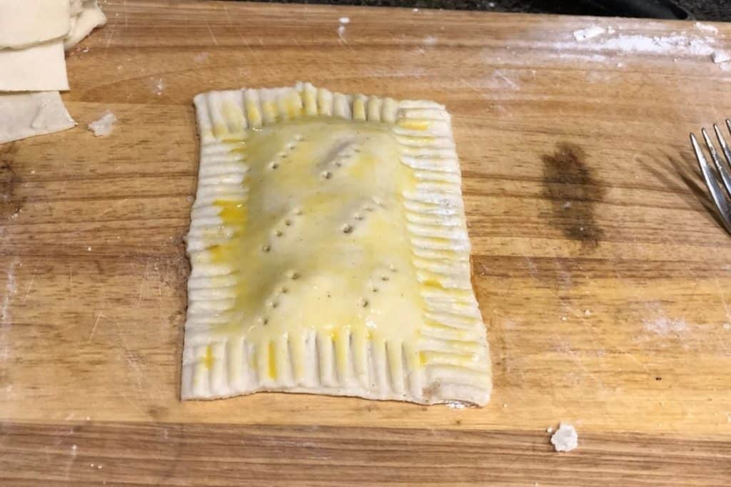 homemade brown sugar cinnamon pop tart that has not been baked yet. It's assembled on a cutting board and has egg wash and holes poked in the top for venting.