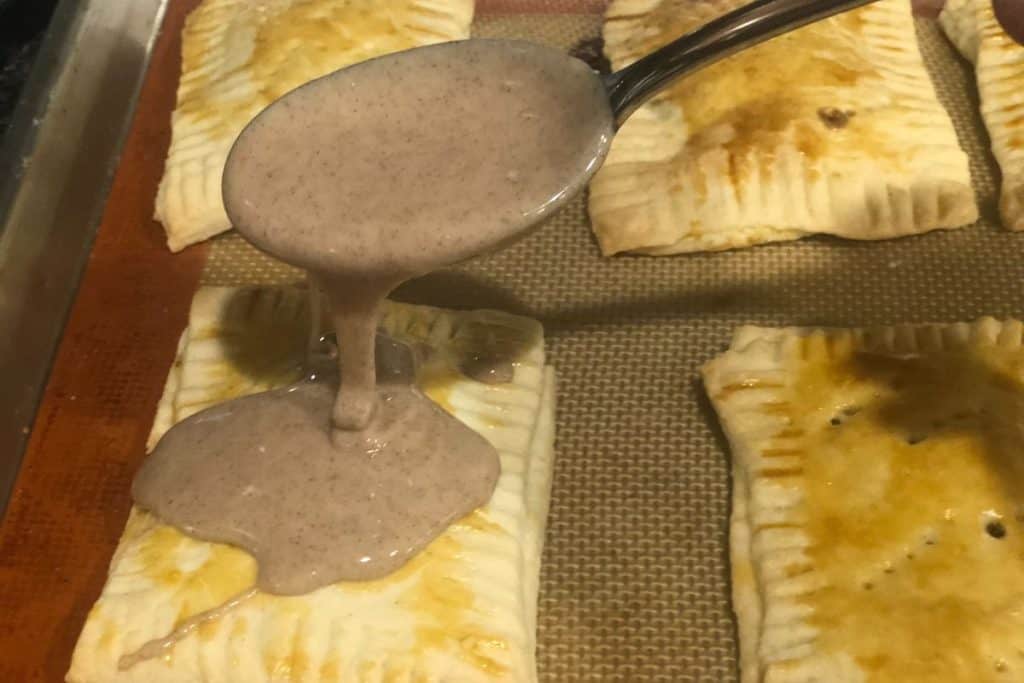 A spoon drizzling icing onto homemade brown sugar cinnamon pop tarts