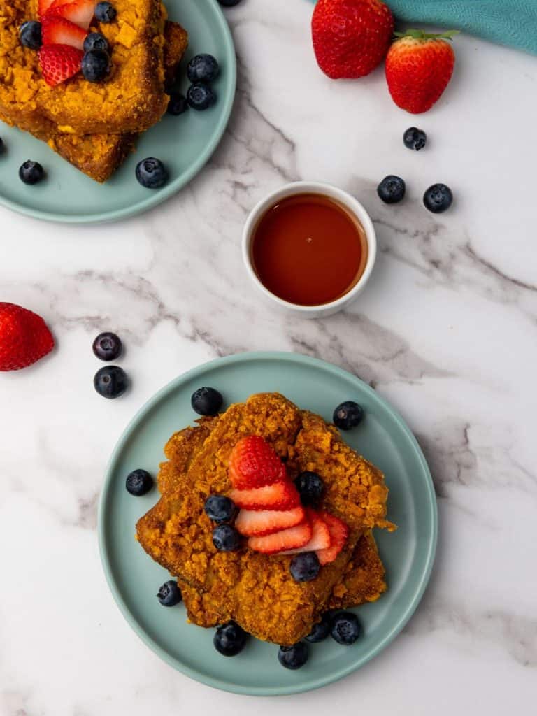 A zoomed out view of Captain Crunch French Toast served on a plate with strawberries and blueberries