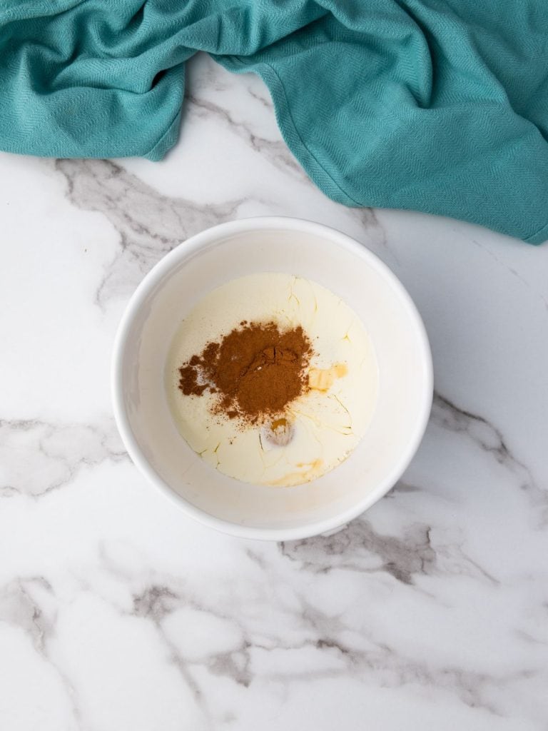 Egg mixture in a white bowl with vanilla, sugar, cream and cinnamon added to the eggs.