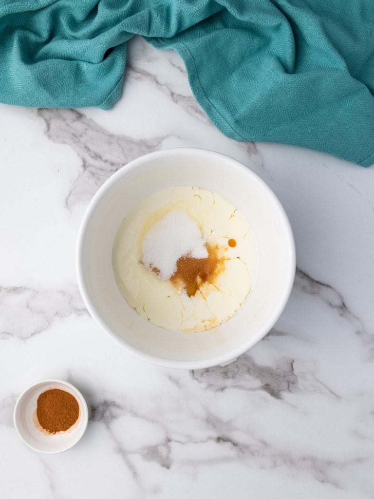 Egg mixture in a white bowl with vanilla, cream, and sugar added to the eggs.