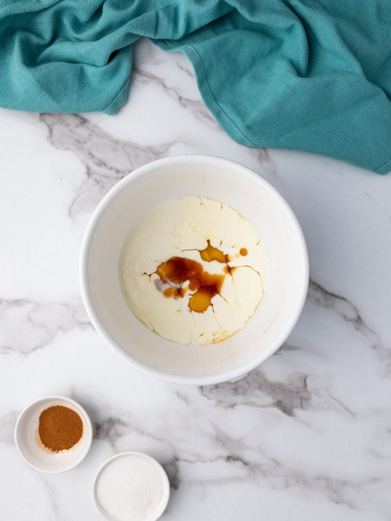 Egg mixture in a white bowl with vanilla and cream added to the eggs.