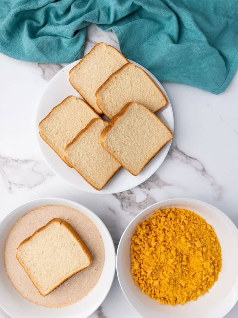 A breading station for the French toaast recipe with a platter of bread, the egg batter and a bowl of crushed up captain crunch cereal.