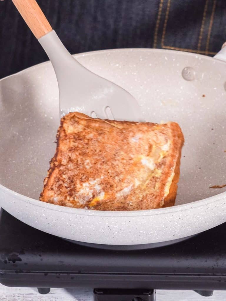 A gray frying pan and a piece of French toast is being flipped in it.
