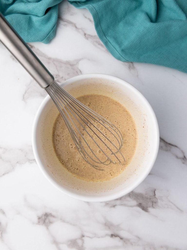 French toast egg mixture in a white bowl with a whisk all mixed together.