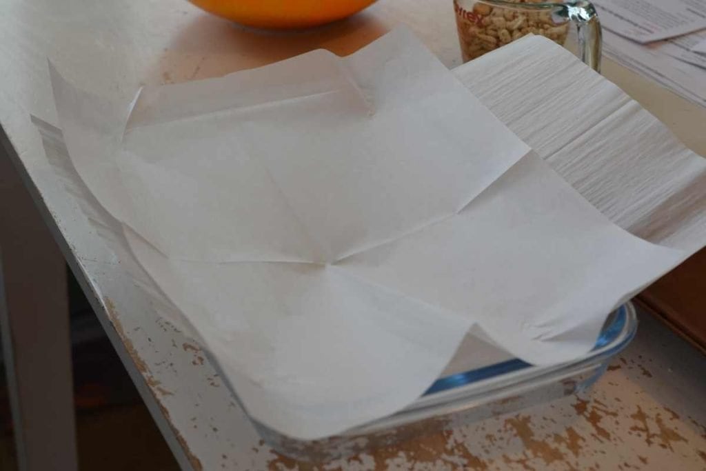 A glass 9x13 baking dish lined with parchment paper for prep in making granola bars