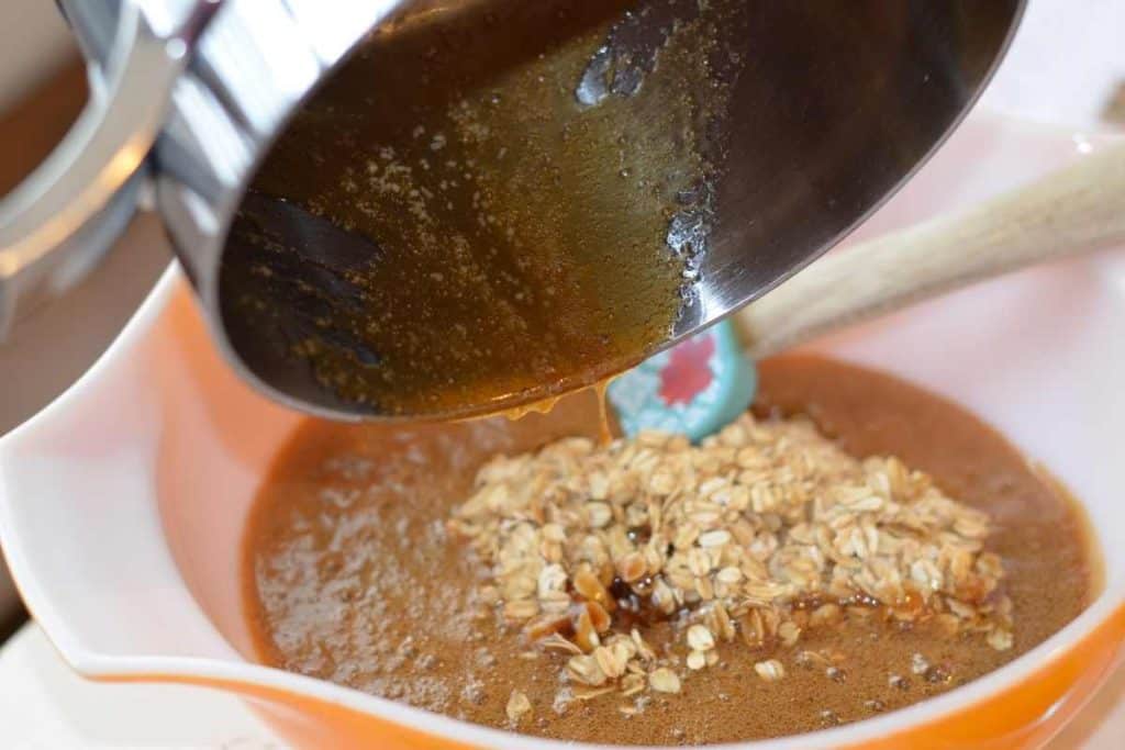Pouring the brown sugar syrup from a pan into a bowl with toasted oats to make granola bars