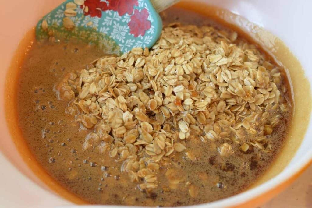 Toasted oats with the brown sugar syrup poured over them in a bowl with a spatula