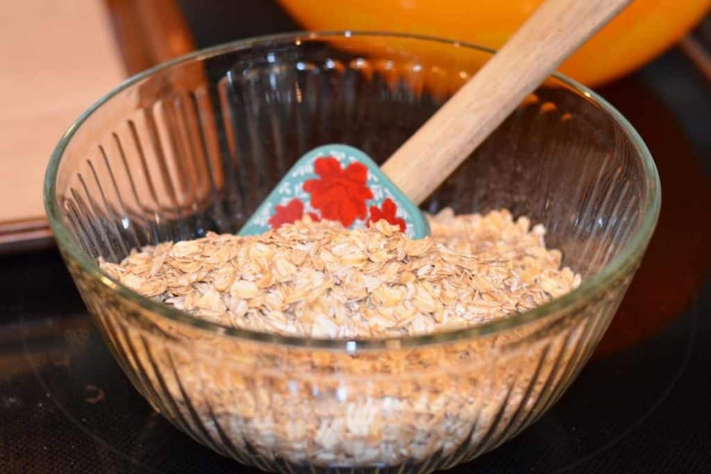 A glass bowl of oatmeal with a blue spatula in the bowl.