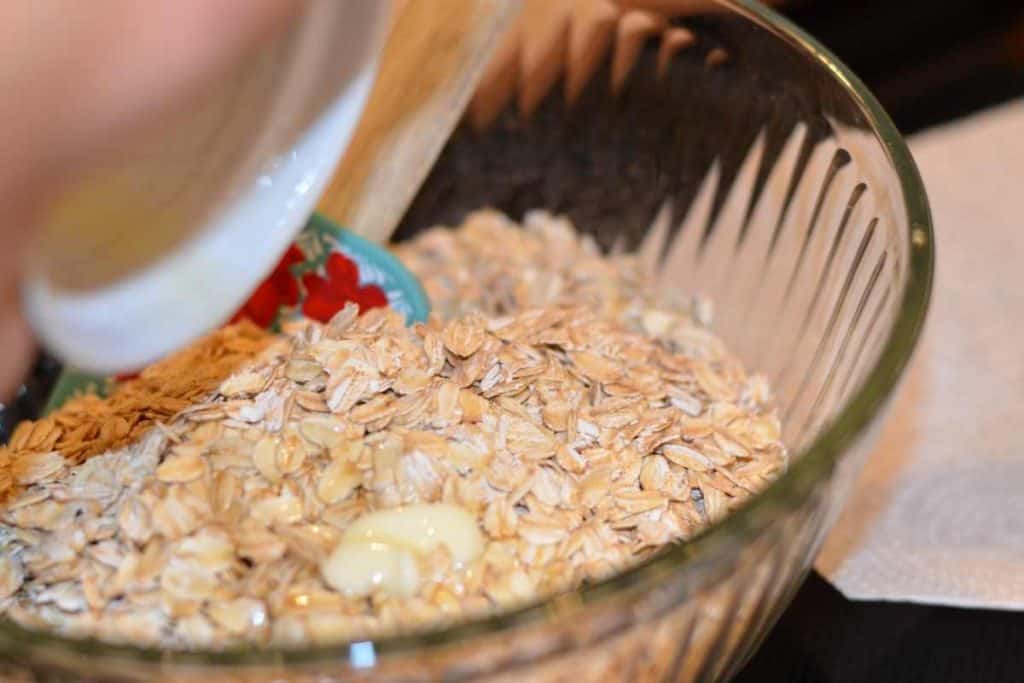 melted butter poured over oats in a glass bowl that are ready to be mixed together
