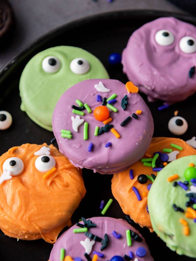 Close-up of colorful Halloween chocolate covered Oreos decorated with spooky sprinkles and candy eyes.