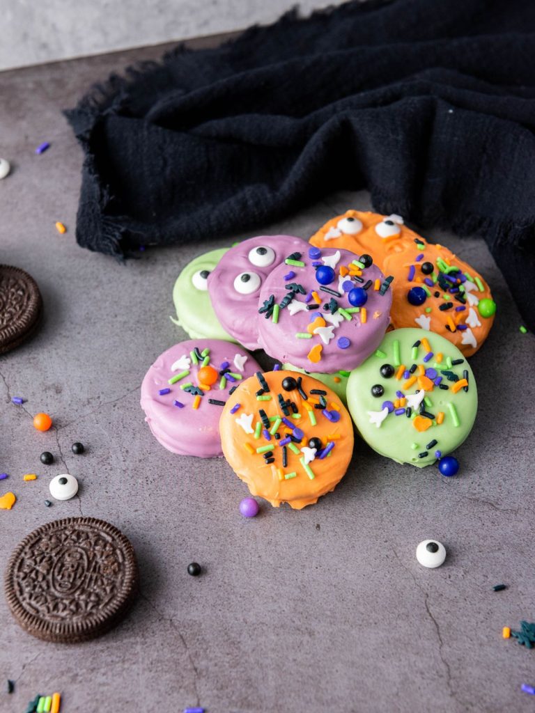 Halloween Oreos in bright colors with sprinkles arranged on a dark background for a festive party look.