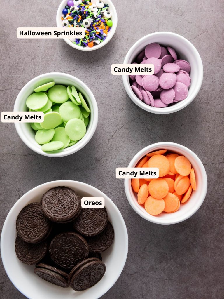 Ingredients for Halloween Chocolate Covered Oredos including bowls of Oreos, purple, green, and orange candy melts with colorful Halloween sprinkles