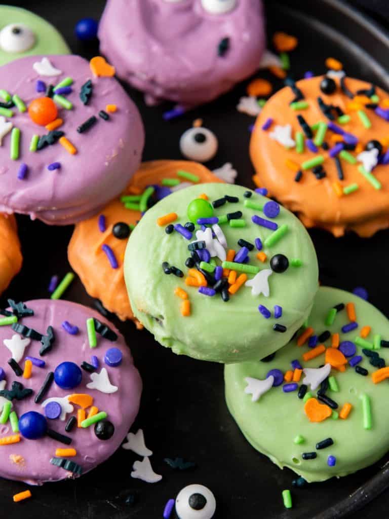 Close-up of colorful Halloween chocolate covered Oreos decorated with spooky sprinkles and candy eyes.